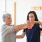 Physical therapist helping elderly woman with arm raises.