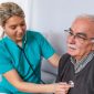 Nurse using stethoscope on elderly male patient.